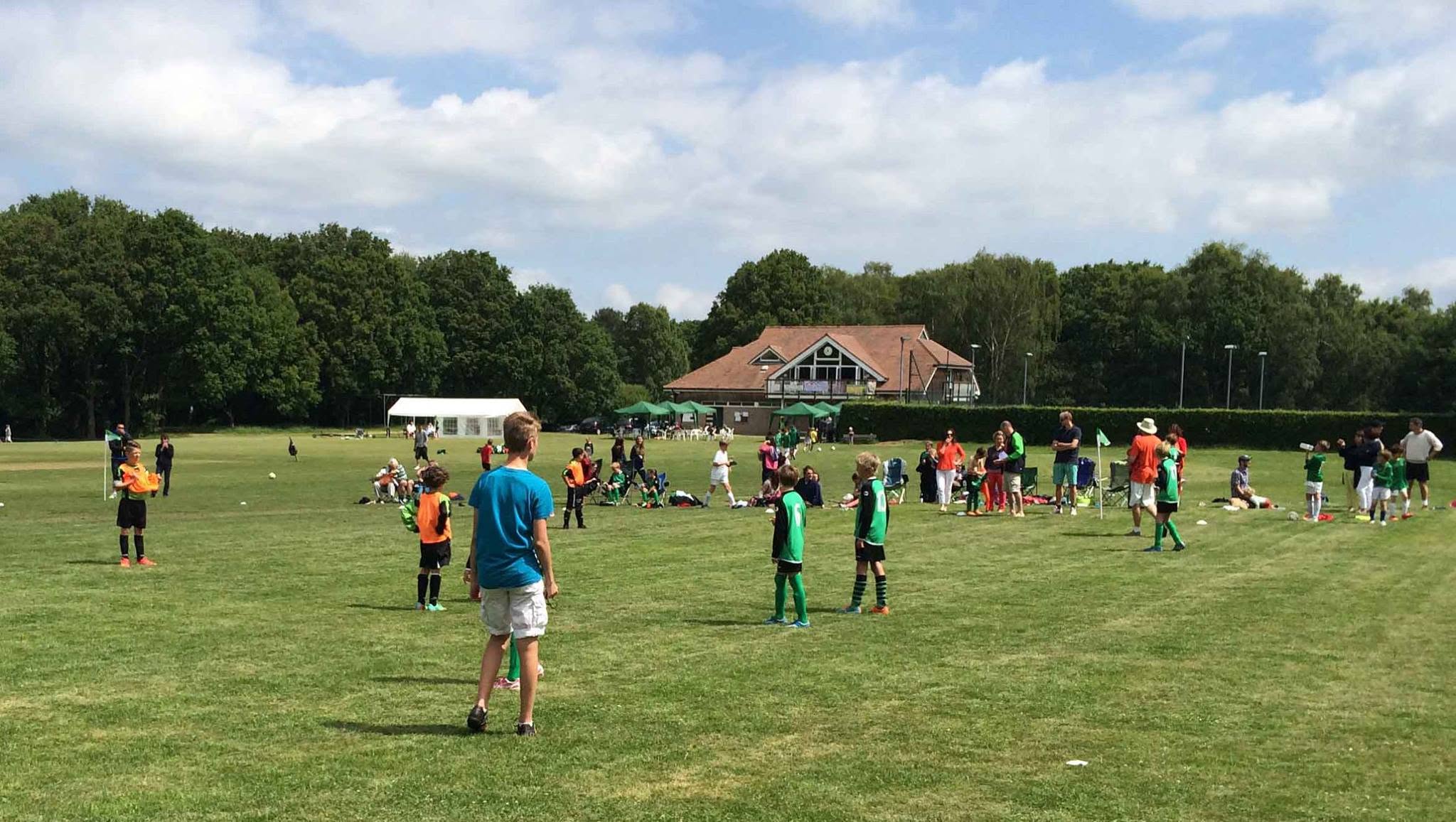 Young Forest Row Junior FC players at a tournament day on the Memorial Pavilion ground, with the pavilion and a marquee visible in the background