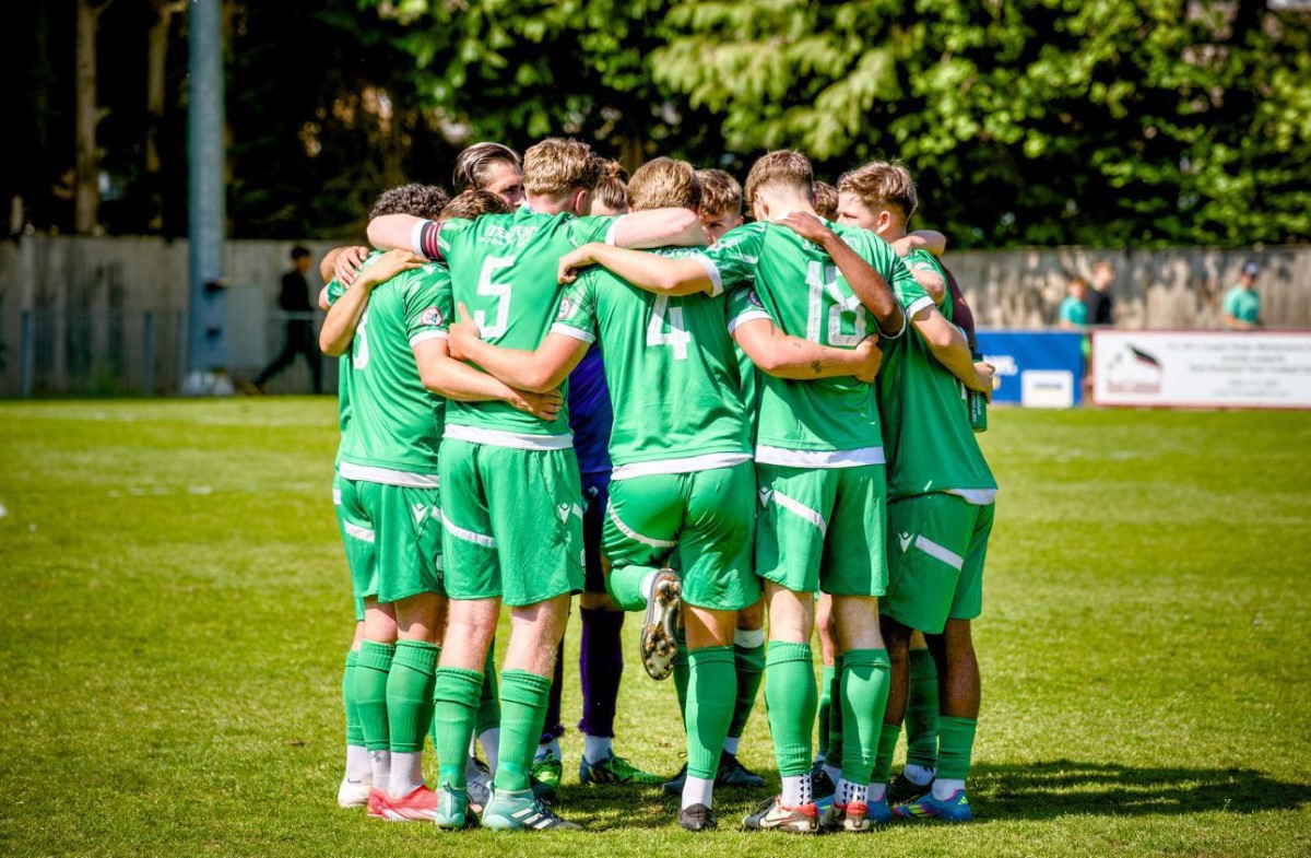 Forest Row FC players in a pre-match huddle in green shirts, arms around each other