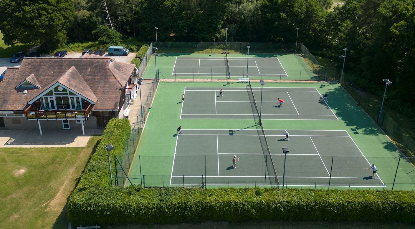 Aerial view of the Memorial Pavilion and the three all-weather tennis courts at Forest Row sports ground, surrounded by trees